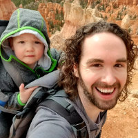 Jake Rome smiling big, carrying his child on his back