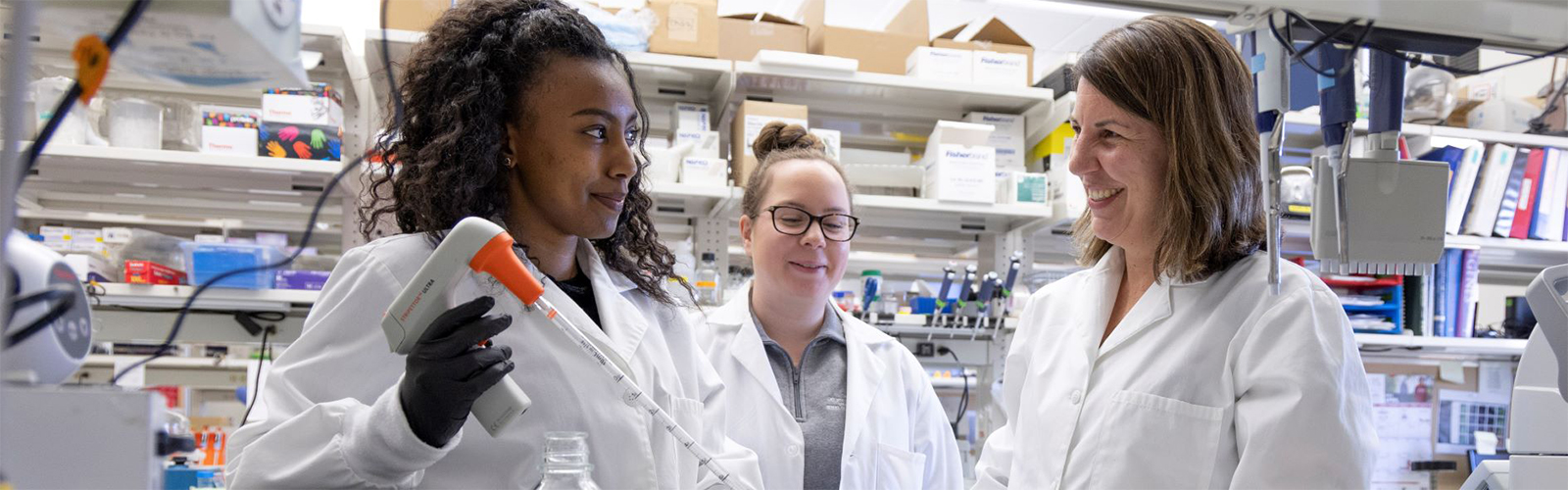Two young researchers and a faculty member at a lab bench using a pipette