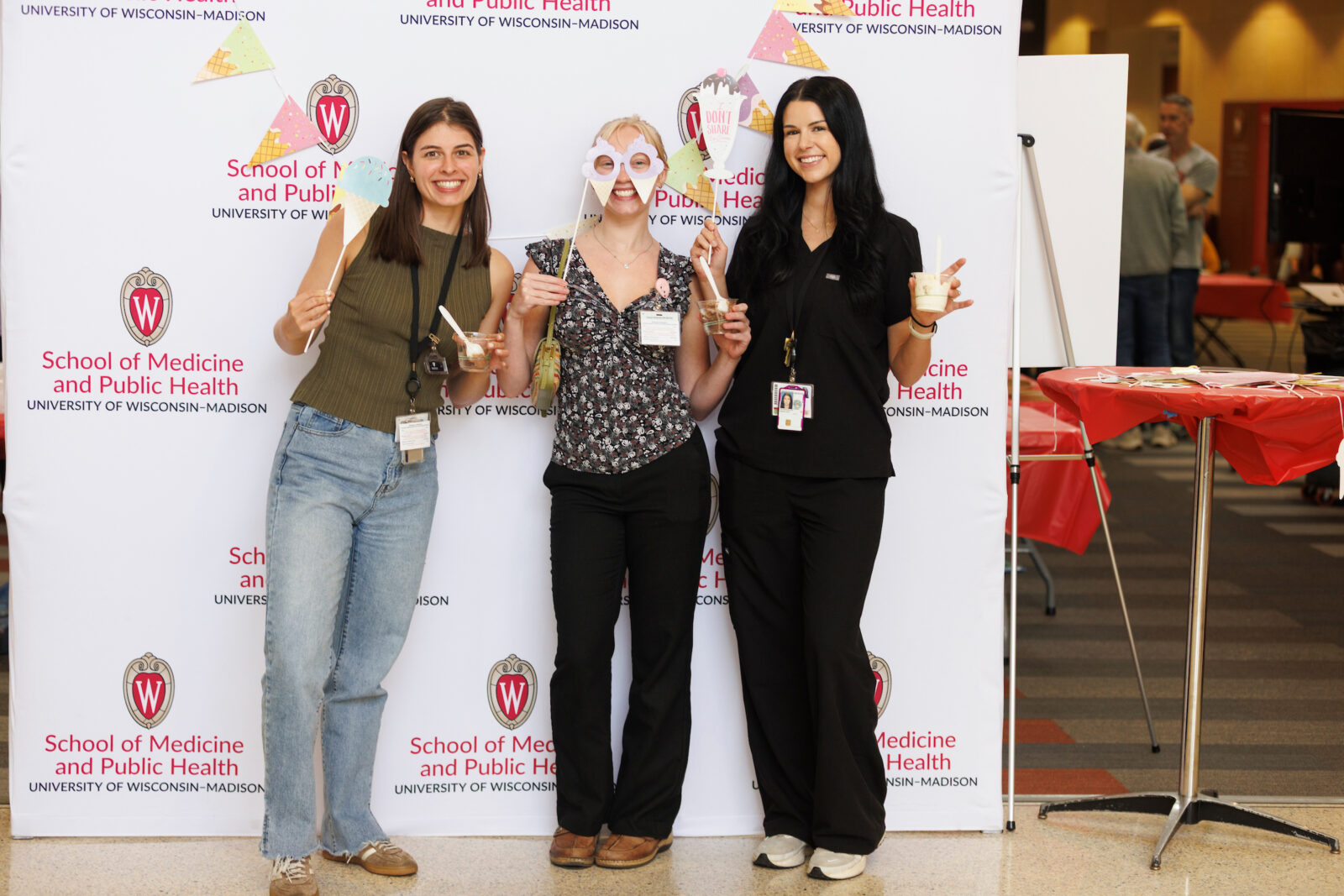 Students hold props and ice cream behind SMPH photo wall.
